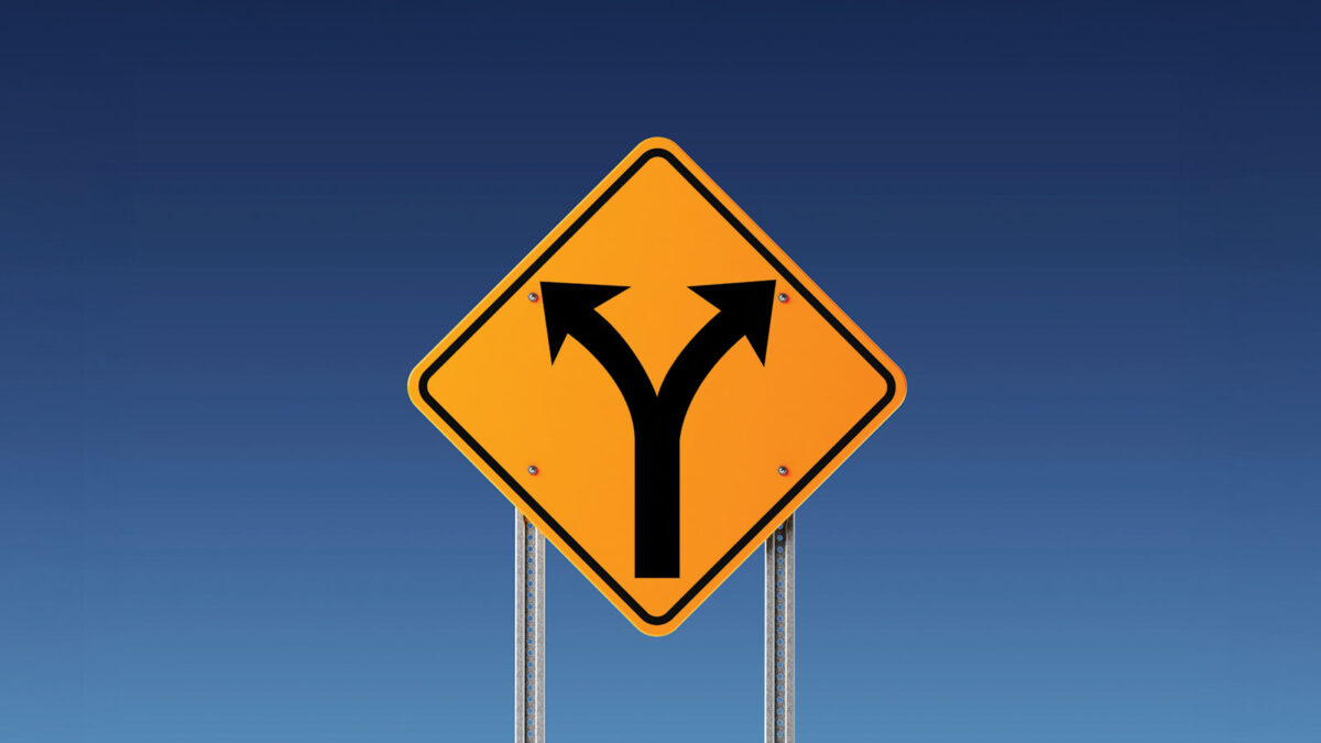 Yellow road sign with two black arrows pointing left and right with blue sky in background