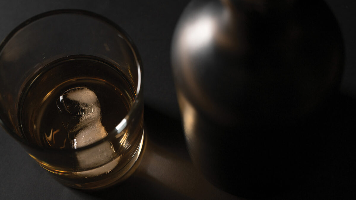 A glass of whiskey standing next to a black bottle