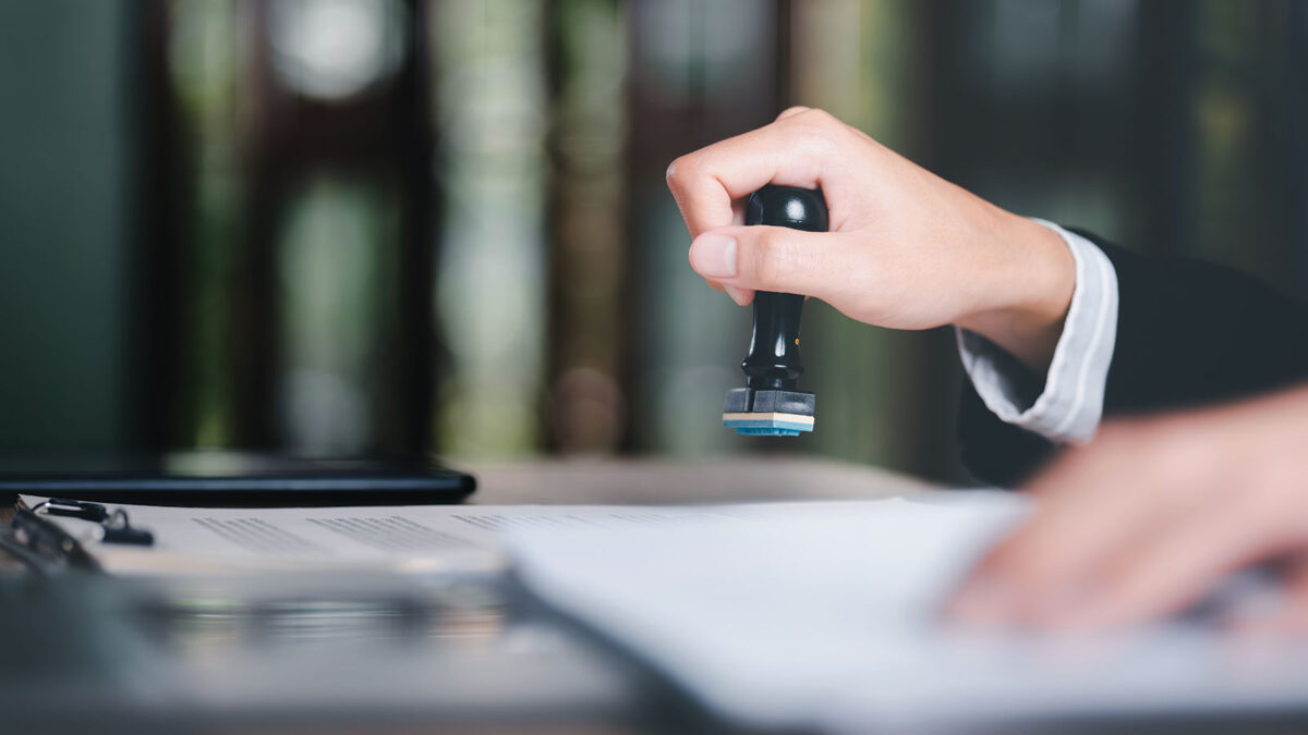 A young executive is stamping on documents for a business contract. Transaction and document management concepts include negotiating corporate entities and filling out legal forms or agreements.