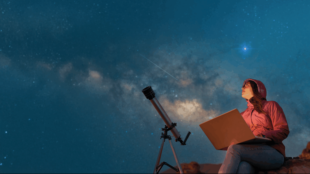 Portrait woman sitting in the desert with a laptop next to a telescope at night watching the starry sky, astronomy and stargazing concept