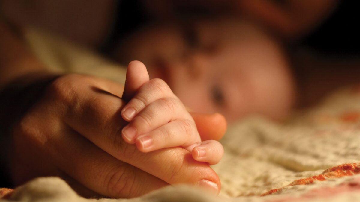 Out of focus baby grabbing adult finger